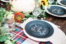 a bright fall table setting with plaid fabric, blakc plates, blooms, greenery and pumpkins looks very cute