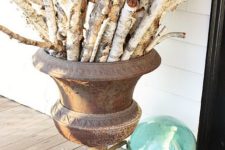 a coastal fall decoration of a large urn, lots of birch branches and seashells and a float next to it