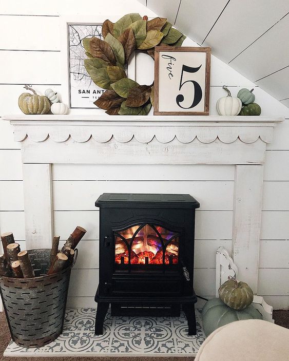 a cozy fall mantel with a large leaf wreath, muted pumpkins and branches in the bucket