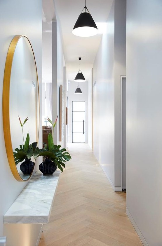 a long white Scandinavian hallway with black pendant lamps hanging in a row feels airy and lit up