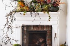 a lush harvest mantel decorated with greenery, long branches and pumpkins and gourds on the mantel