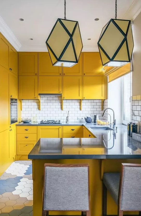 a mustard kitchen with grey stone countertops and grey stools, a white subway tile backsplash and geometric pendant lamps