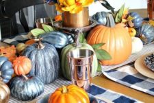 a navy and copper fall tablescape with painted pumpkins, a plaid placemat, a lush floral centerpiece