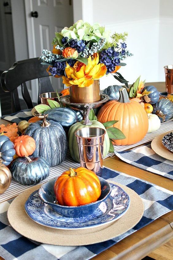 a navy and copper fall tablescape with painted pumpkins, a plaid placemat, a lush floral centerpiece
