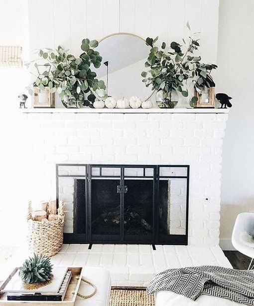 a neutral fal mantel with fresh greenery, white pumpkins, candle lanterns and a basket with branches