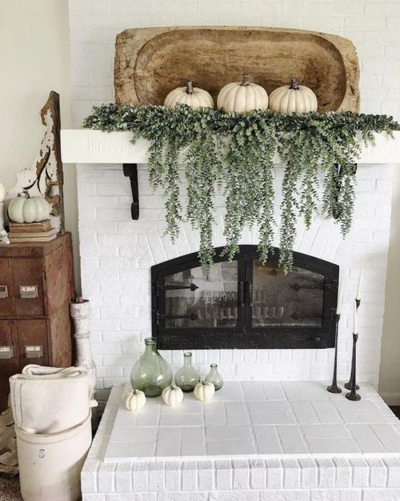 a rustic fall mantel with cascading greenery, white pumpkins with a wooden dough bowl plus green bottles