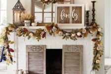 a rustic fall mantel with dried fall leaves and pumpkins, candles in wooden candle holders, wheat arrangements and a rustic sign