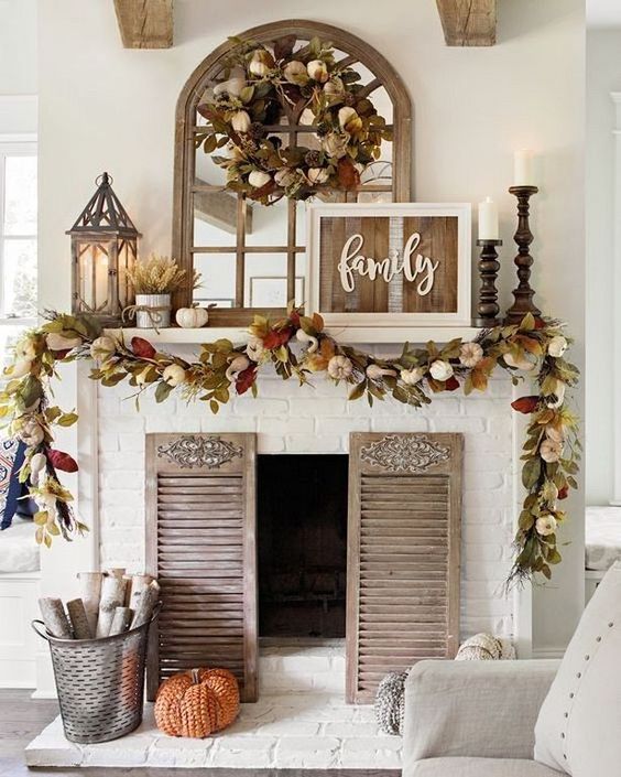 a rustic fall mantel with dried fall leaves and pumpkins, candles in wooden candle holders, wheat arrangements and a rustic sign