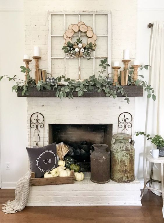 a rustic fall mantel with greenery, candles in wooden candleholders, a crate with white pumpkins, a pillow and a wood slice wreath
