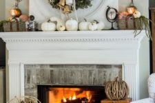 a rustic fall mantel with white pumpkins, baskets with faux pumpkins, a greenery wreath with bells and vine pumpkins