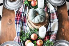 a rustic fall table setting with a plaid runner, pillar candles, heirloom pumpkins, apples, greenery and pinecones