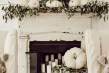 a shabby chic and rustic fall mantel with greenery, white pumpkins, a lush wreath with greenery and candles in the fireplace