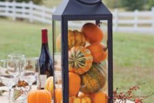 a simple and chic fall decoration of a black lantern filled with gourds and pumpkins