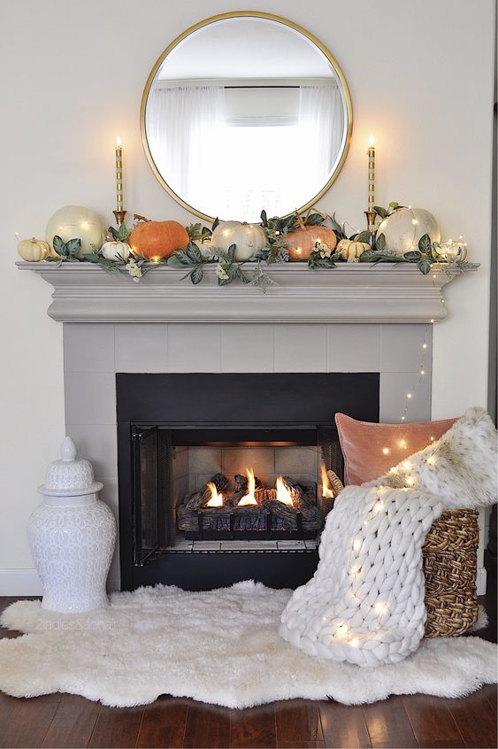 a simple contemporary fall mantel done with greenery and pumpkins of muted colors plus lights all over it