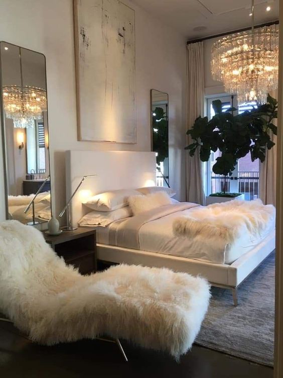 a sophisticated bedroom with a white faux fur lounger and a matching throw on the bed is all glam and chic