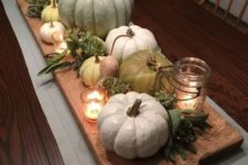 a stylish natural fall centerpiece of a cuttin board, heirloom pumpkins, greenery, candles and dried blooms
