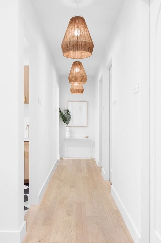 a white long and narrow hallway is done with wicker pendant lamps and tropical leaves to highlight the ambience