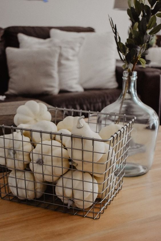 a wire box filled with faux white pumpkins and gourds and a clear vase with dried herbs