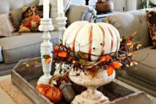 a wooden tray with orange fabric pumpkins, giant acorns and a large painted pumpkin with leaves and berries in an urn