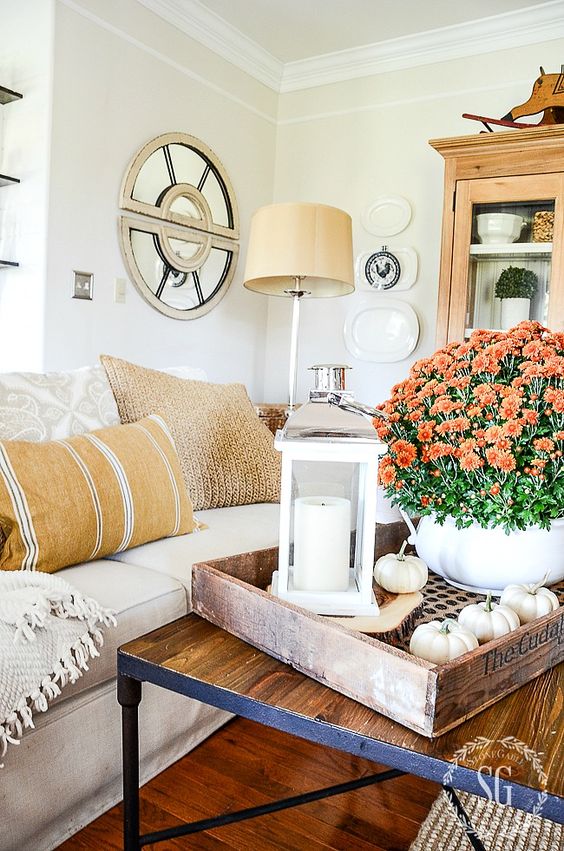 a wooden tray with white pumpkins, a white candle lantern and bright fall blooms in a white pot