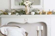 an elegant fall mantel decorated with fresh greenery, fabric and porcelain pumpkins and white roses in a metallic vase