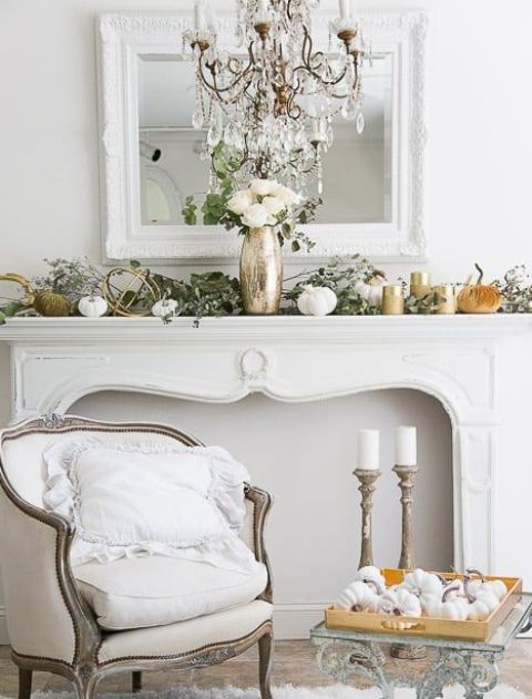 an elegant fall mantel decorated with fresh greenery, fabric and porcelain pumpkins and white roses in a metallic vase