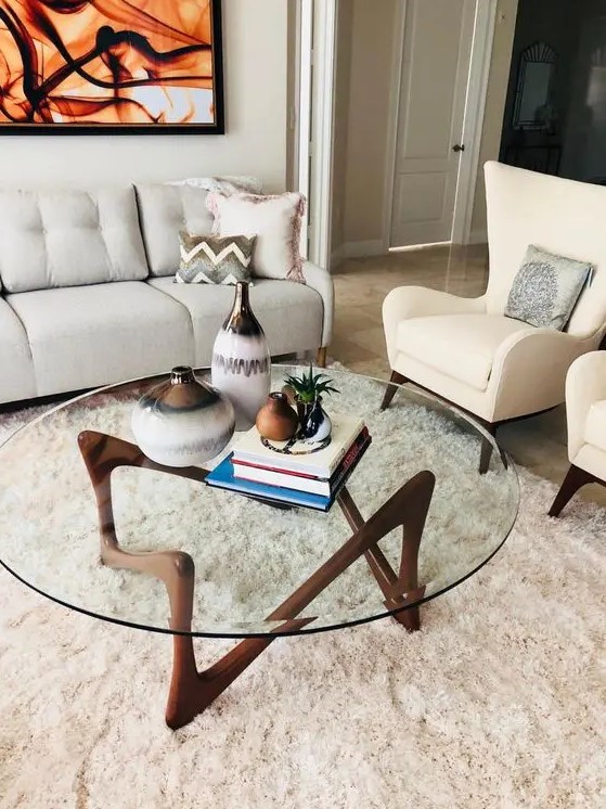 an eye-catchy mid-century modern coffee table with a round clear glass tabletop and a quirky dark stained wooden base is wow