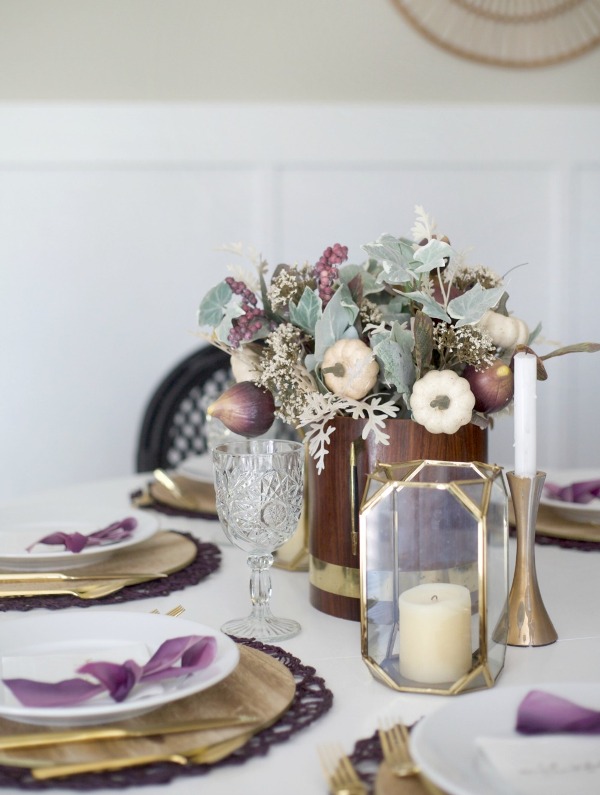 a Thanksgiving table setting with plywood placemats and a gold faceted candleholder, purple placemats and bows, purple veggies and berries