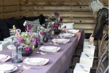 a Thanksgiving tablescape with a lilac tablecloth, bold purple and lilac blooms, black and gold vases and gold cutlery