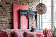 a boho living room with a brick wall, a pink sofa with printed pillows, a matching ottoman, a rattan pendant lamp and a Moroccan rug