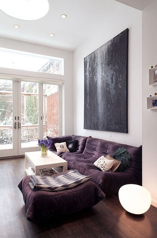 a bold modern living room with a low purple sofa and a large pouf, a white table and an oversized black artwork