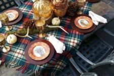 a bright Thanksgiving table with antlers, pumpkins, pinecones, a plaid tablecloth and a fall leaf arrangement