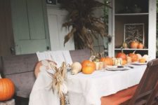 a bright fall tablescape with a white and an orange tablecloth, pumpkins, corn cobs and plates and placemats