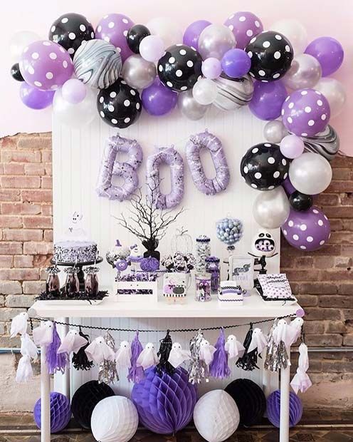 a catchy Halloween sweets table in black, white and purple, with a balloon garland and balloons letters plus a ghost bunting and some paper balls