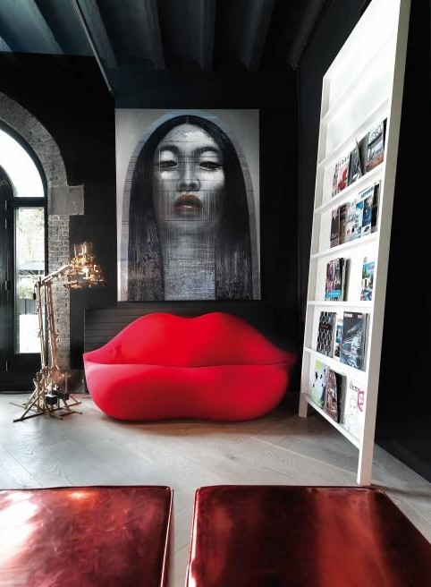 a catchy living room with dark walls, a creative ledge storage unit and ared lip shaped sofa and a bold artwork