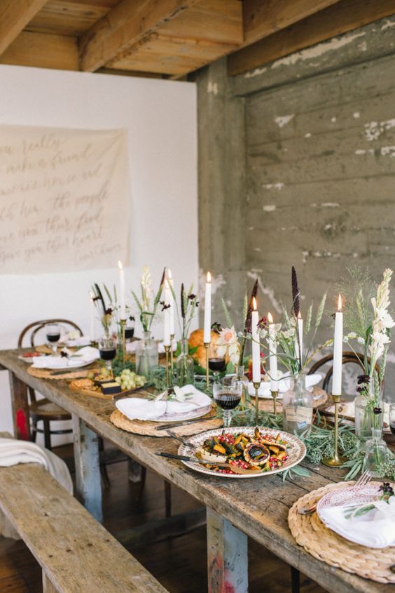a chic Thanksgiving tablescape with woven placemats, tall candles, a greeneyr runner and some pumpkins