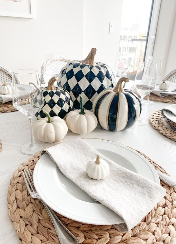 a chic modern farmhouse Thanksgiving tablescape with blakc and white pumpkins, woven placemats, neutral linens and glasses