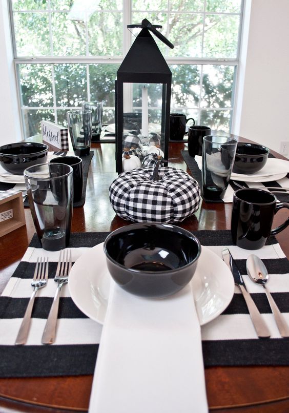 a cool black and white Thanksgiving table with striped placemats, black bowls and mugs, buffalo check pumpkins