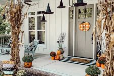 a cozy rustic Halloween porch with dried corn husks, pumpkins, pumpkin planters with blooms and witches’ hats