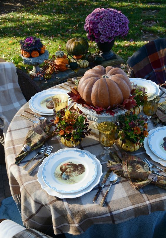 a cozy traditional Thanksgiving table with plaid textiles, bright blooms, printed plates and a pumpkin centerpiece