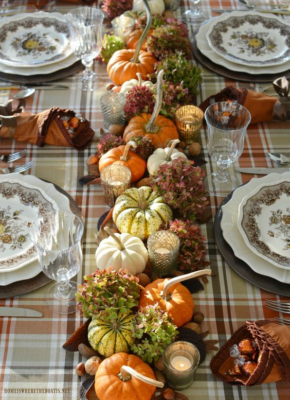 a cozy vintage rustic Thanksgiving tablescape with a plaid tablecloth, printed plates, natural pumpkins, leaves and hydrangeas, candles and nuts