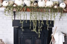 a farmhouse mantel with cascading greenery, lots of pumpkins, spiders, dried grasses and a broom