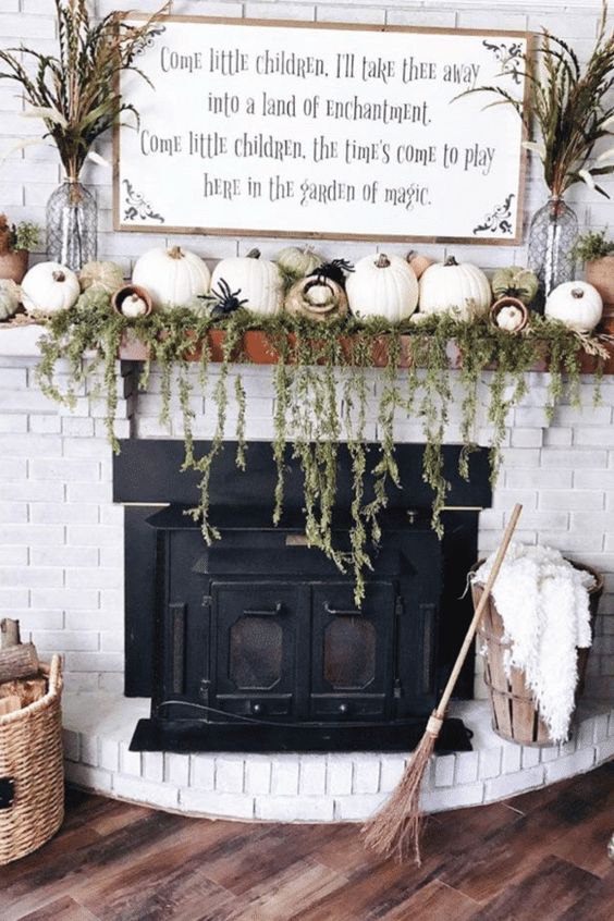 a farmhouse mantel with cascading greenery, lots of pumpkins, spiders, dried grasses and a broom