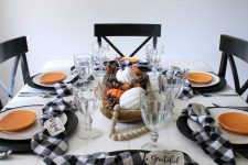 a lovely Thanksgiving tablescape in black and white, with ornage pumpkin plates, beads, a centerpiece of pinecones and pumpkins