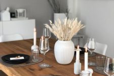 a minimalist monochromatic Thanksgiving tablescape with black plates, grey placemats, candles and bunny tails in a vase