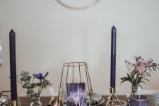 a modern and fresh purple Thanksgiving tablescape with purple candles, blooms and a table number, a deep purple table runner and gold cutlery