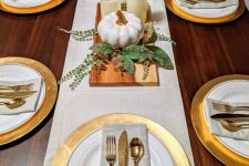 a modern rustic Thanksgiving tablescape with gold chargers, neutral linens, white candles and pumpkins and some greenery