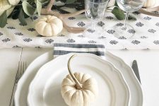 a natural and chic Thankgiving tablescape in white with elegant porcelain, pumpkins, candles, greenery and printed textiles