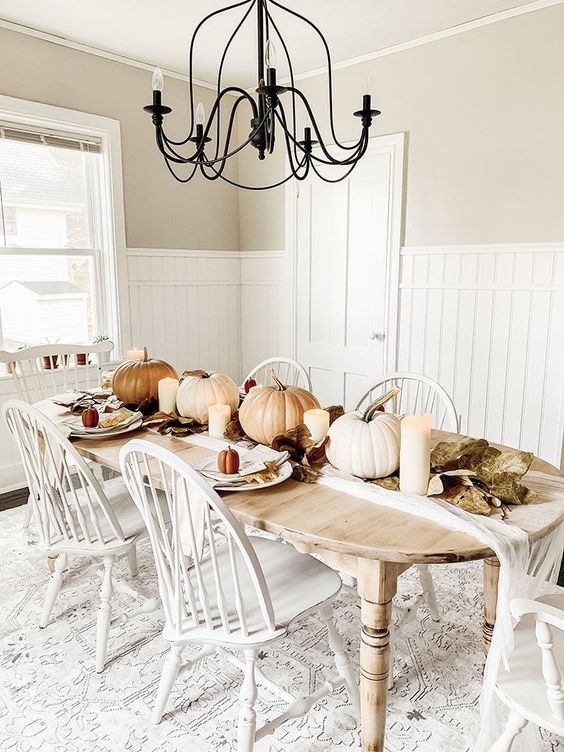 a neutral rustic vintage Thanksgiving table with neutral pumpkins, candles, leaves and simple white porcelain