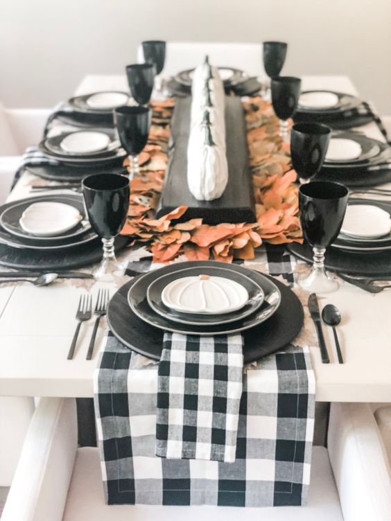 a pretty modern rustic Thanksgiving tablescape with black plates, buffalo check linens, fall leaves, small white pumpkins